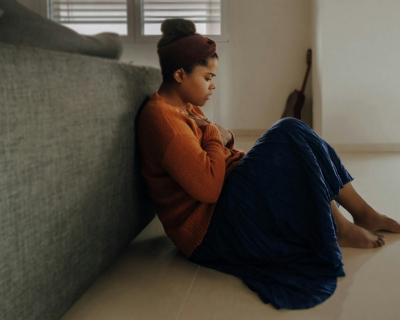 A woman sitting on the floor against her sofa, arms folded in