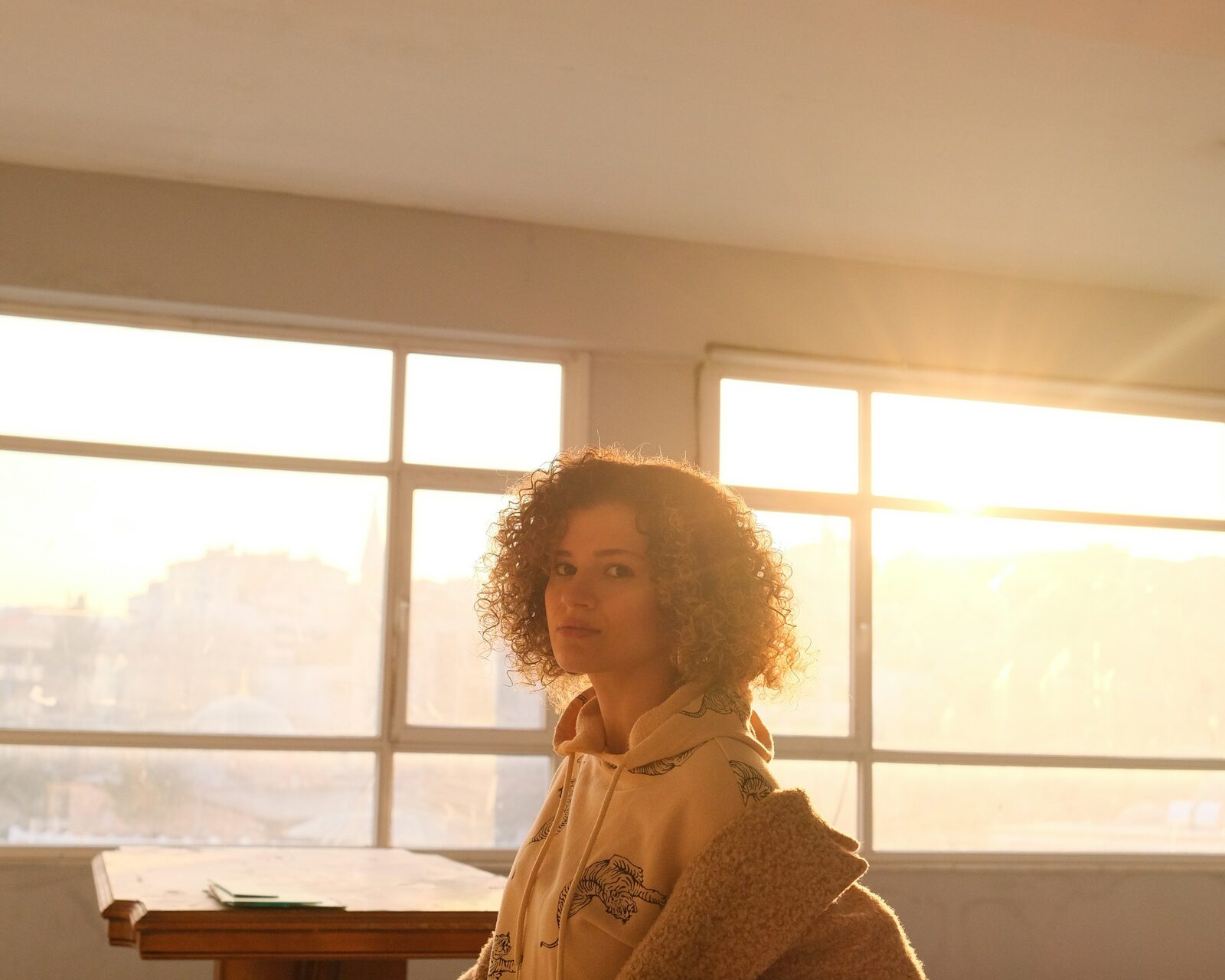 A woman at a table by a window, looking out at the evening light
