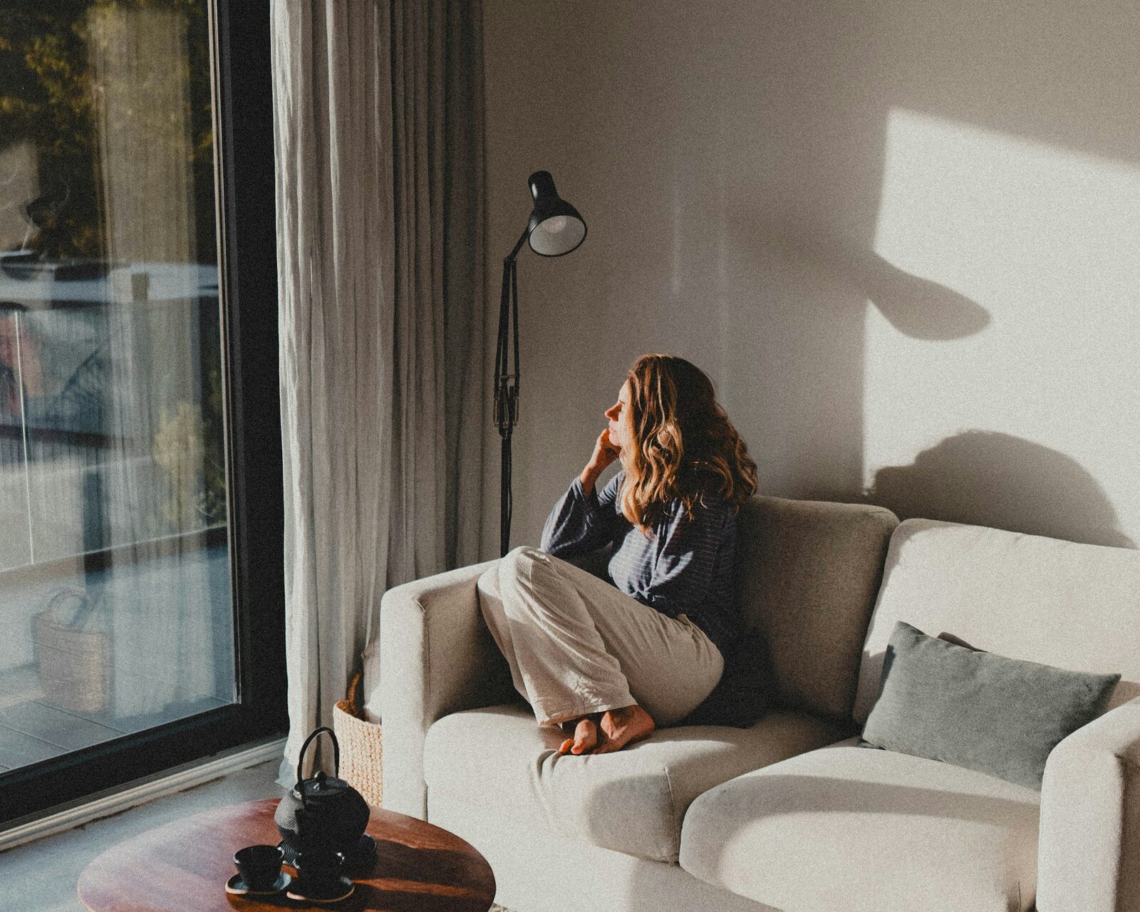A woman alone on a sofa in a large, light-filled room